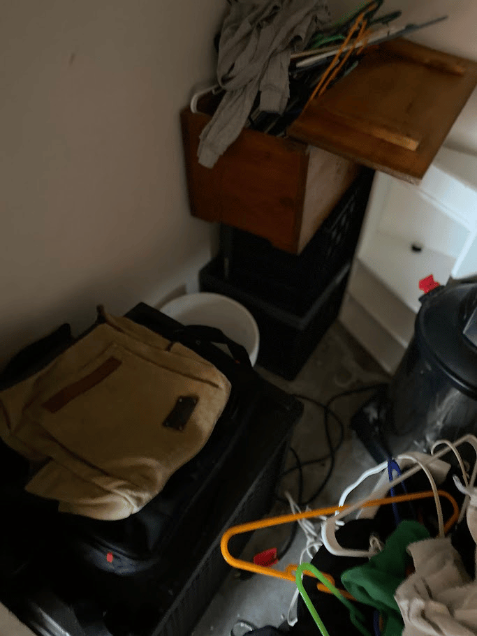 Closet space cluttered with storage bins, dresser drawers, vacuum, cords, and hangers