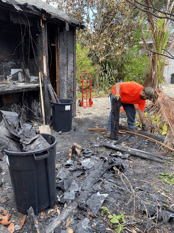 Worker removing charred debris near a burned outdoor structure