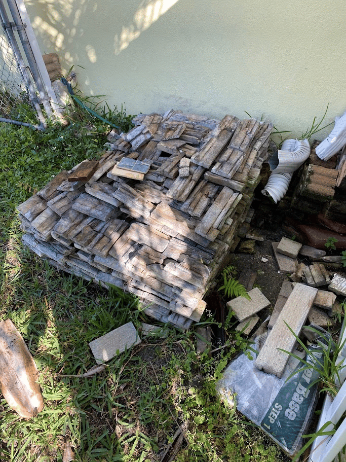 Pile of stone pavers stacked beside a house in a grassy area