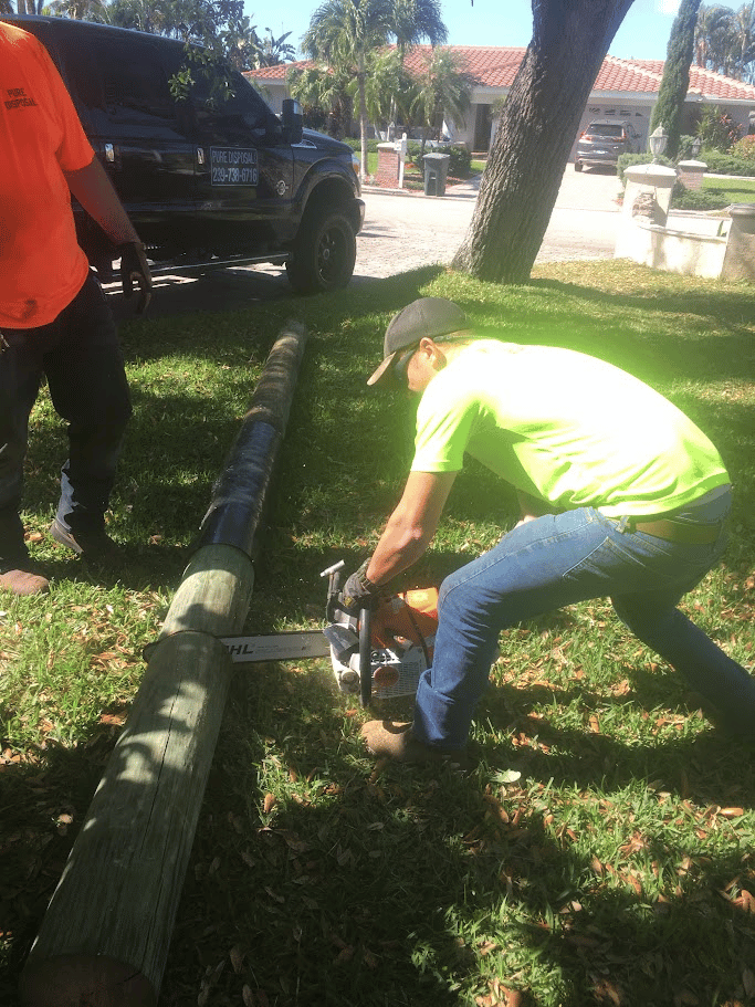 Crew cutting a wooden utility pole during residential debris removal